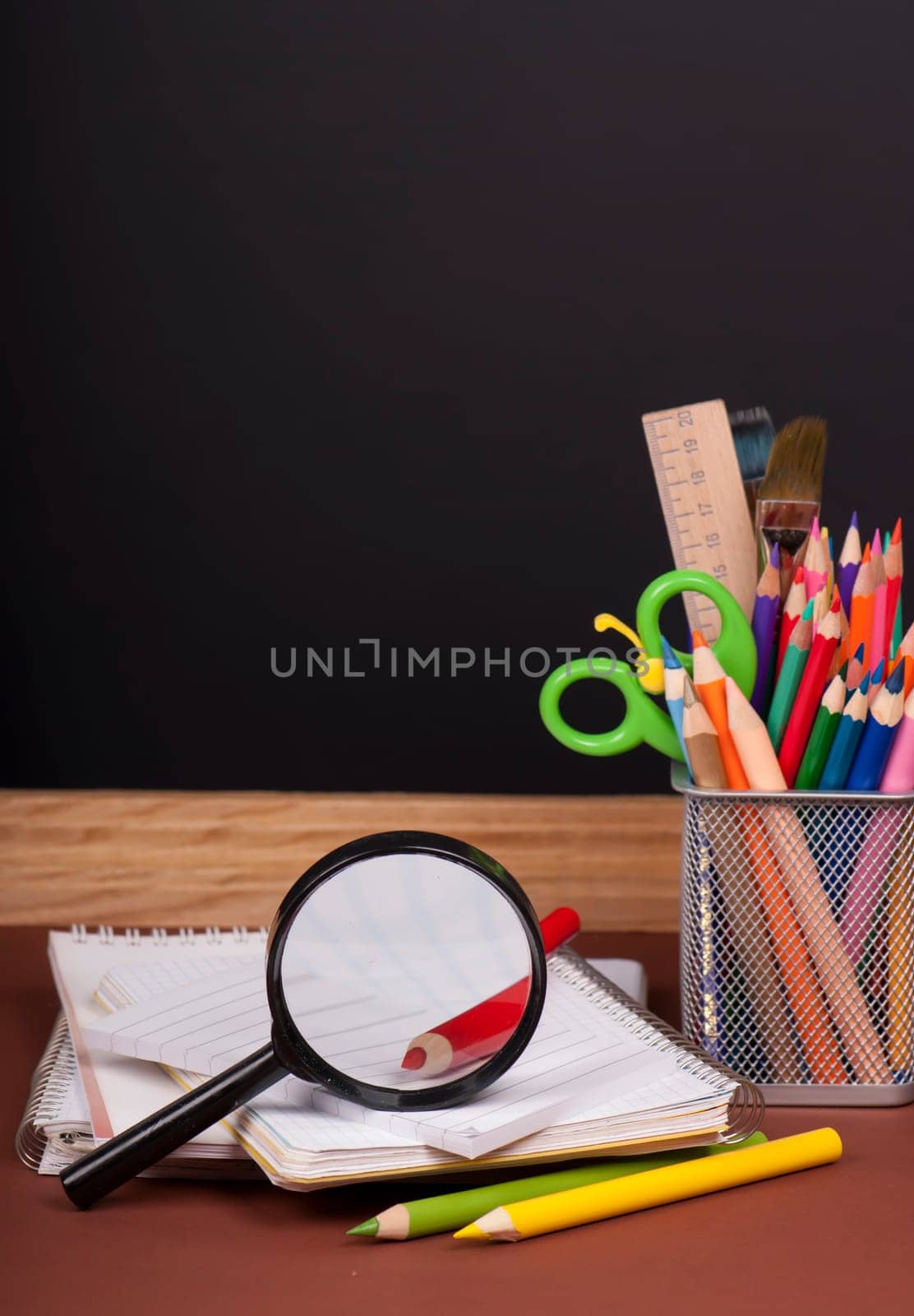 Magnifying glass, scissors, colored paper, textbooksboard, books, pencils, opened empty notebook against a dark background by aprilphoto