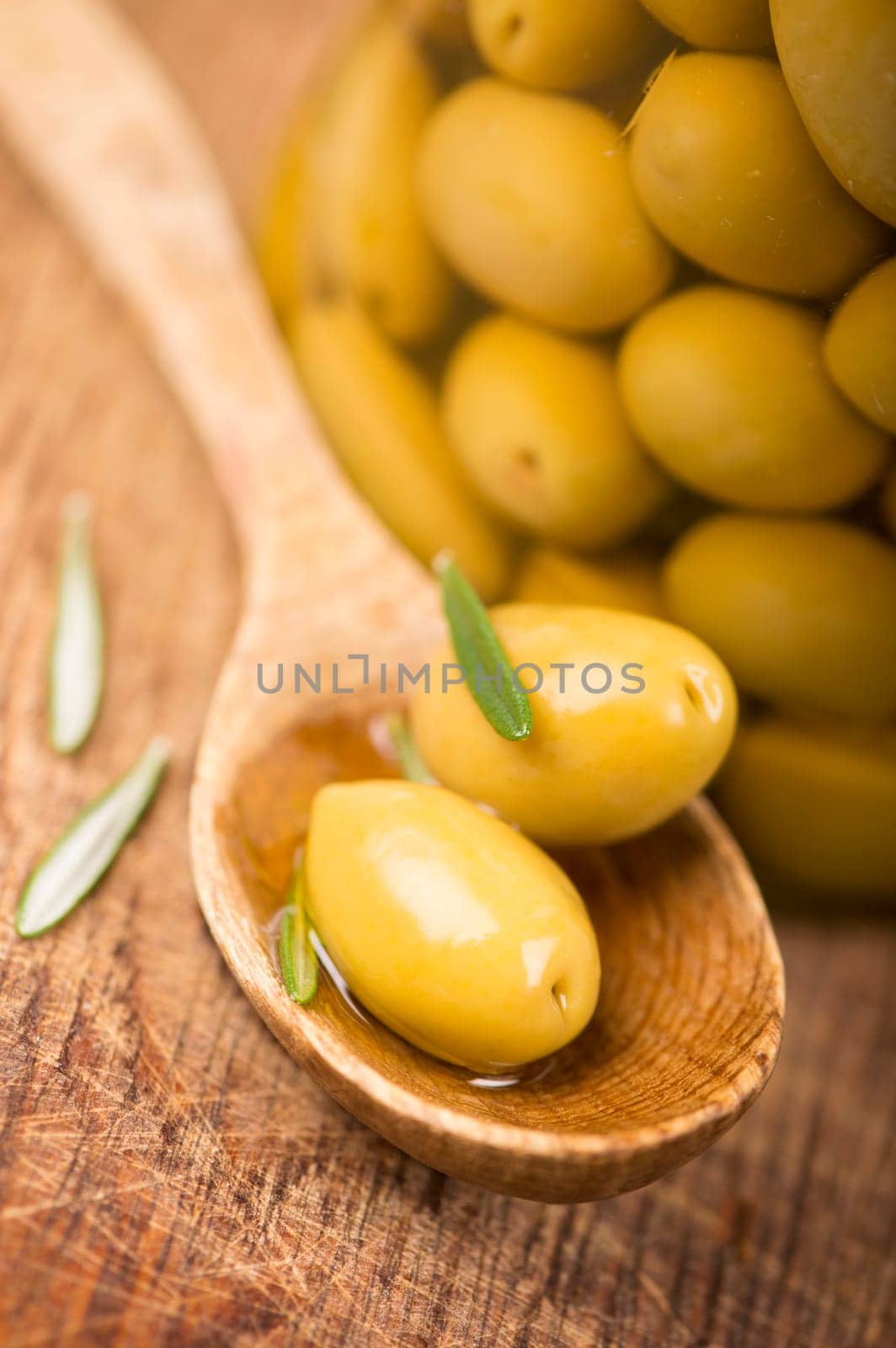 Close up green olives in bank, rosemary on a wooden background