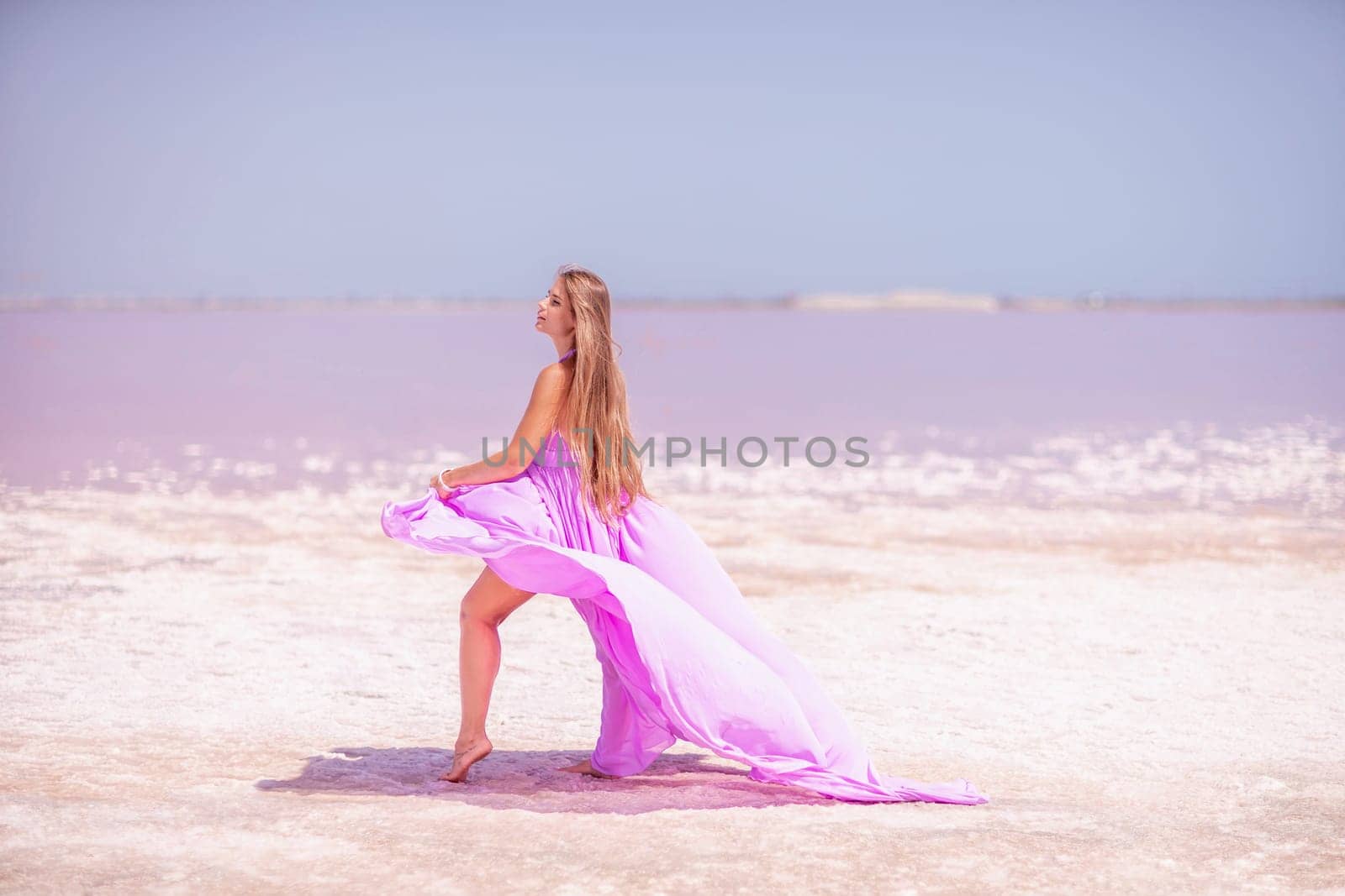 Woman pink salt lake. Against the backdrop of a pink salt lake, a woman in a long pink dress takes a leisurely stroll along the white, salty shore, capturing a wanderlust moment