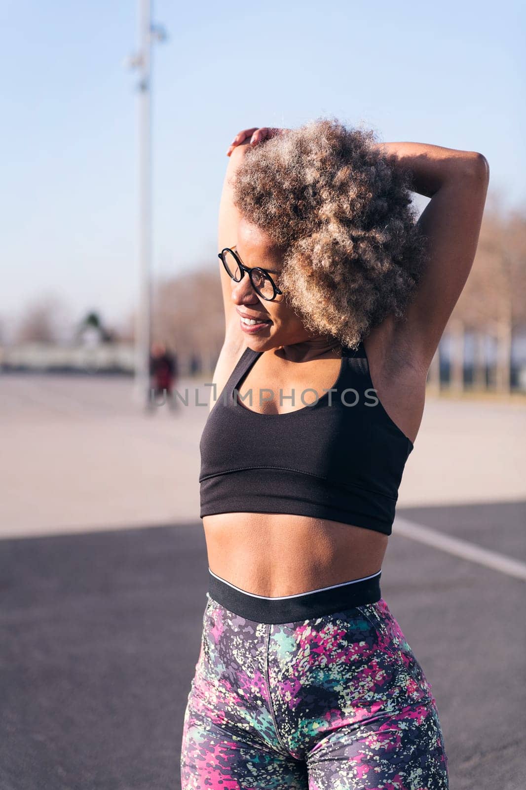 vertical photo of a smiling african american fit woman stretching arms in an urban park, concept of health and sportive lifestyle