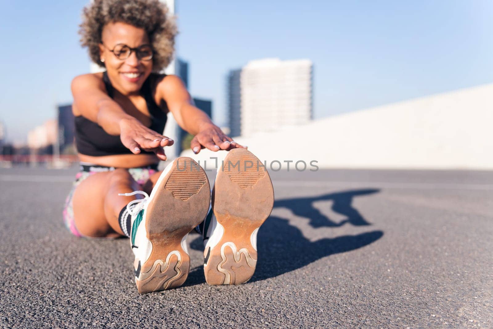 african american woman stretching the legs sitting in an urban park, concept of health and sportive lifestyle, selective focus on the sports shoes and copy space for text