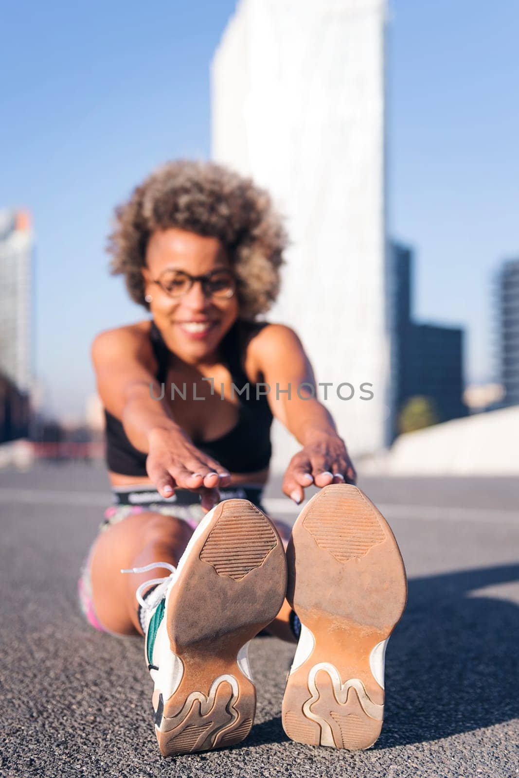 vertical photo of an african american woman stretching the legs sitting in an urban park, concept of health and sportive lifestyle, selective focus on the sports shoes and copy space for text