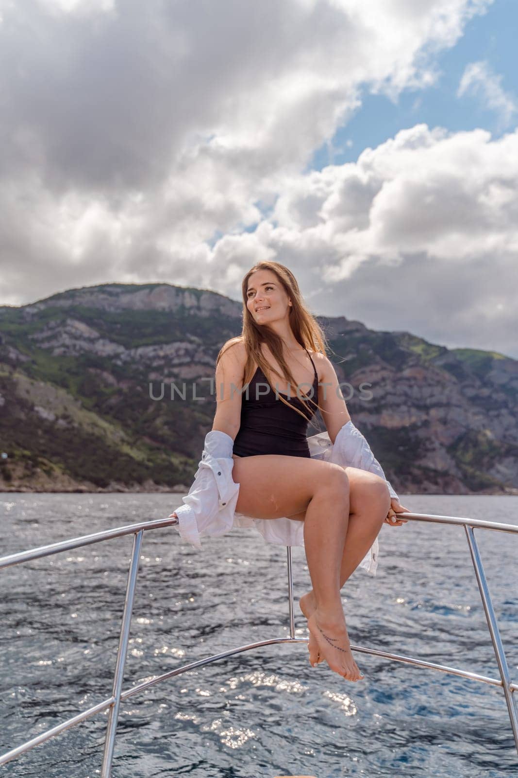 Woman on a yacht. Happy model in a swimsuit posing on a yacht against a blue sky with clouds and mountains.