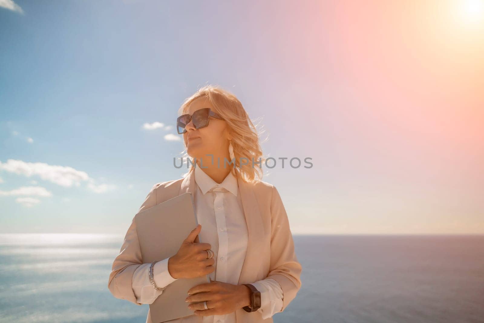 Freelance women sea working on a computer. Pretty middle aged woman with computer and phone outdoors with beautiful sea view. The concept of remote work. by Matiunina