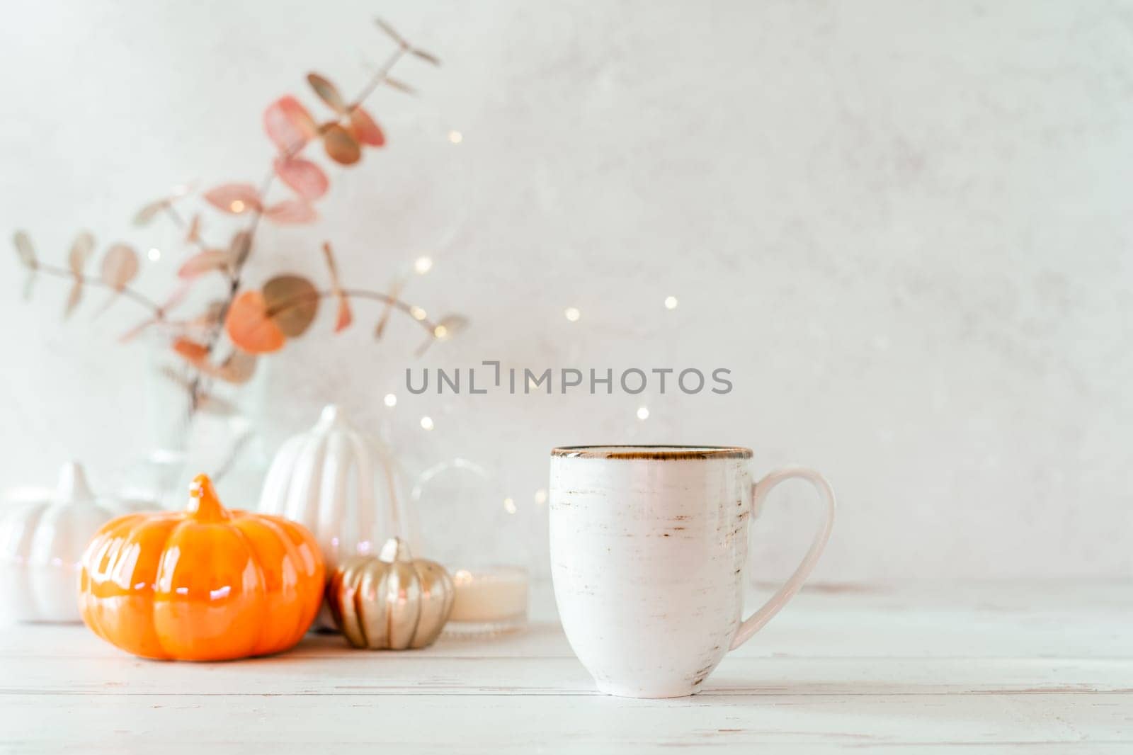 Details of Still life, cup of tea or coffee, pumpkins, candle, brunch with leaves on white table background, home decor in a cozy house. Autumn weekend concept. Fallen leaves and home decoration