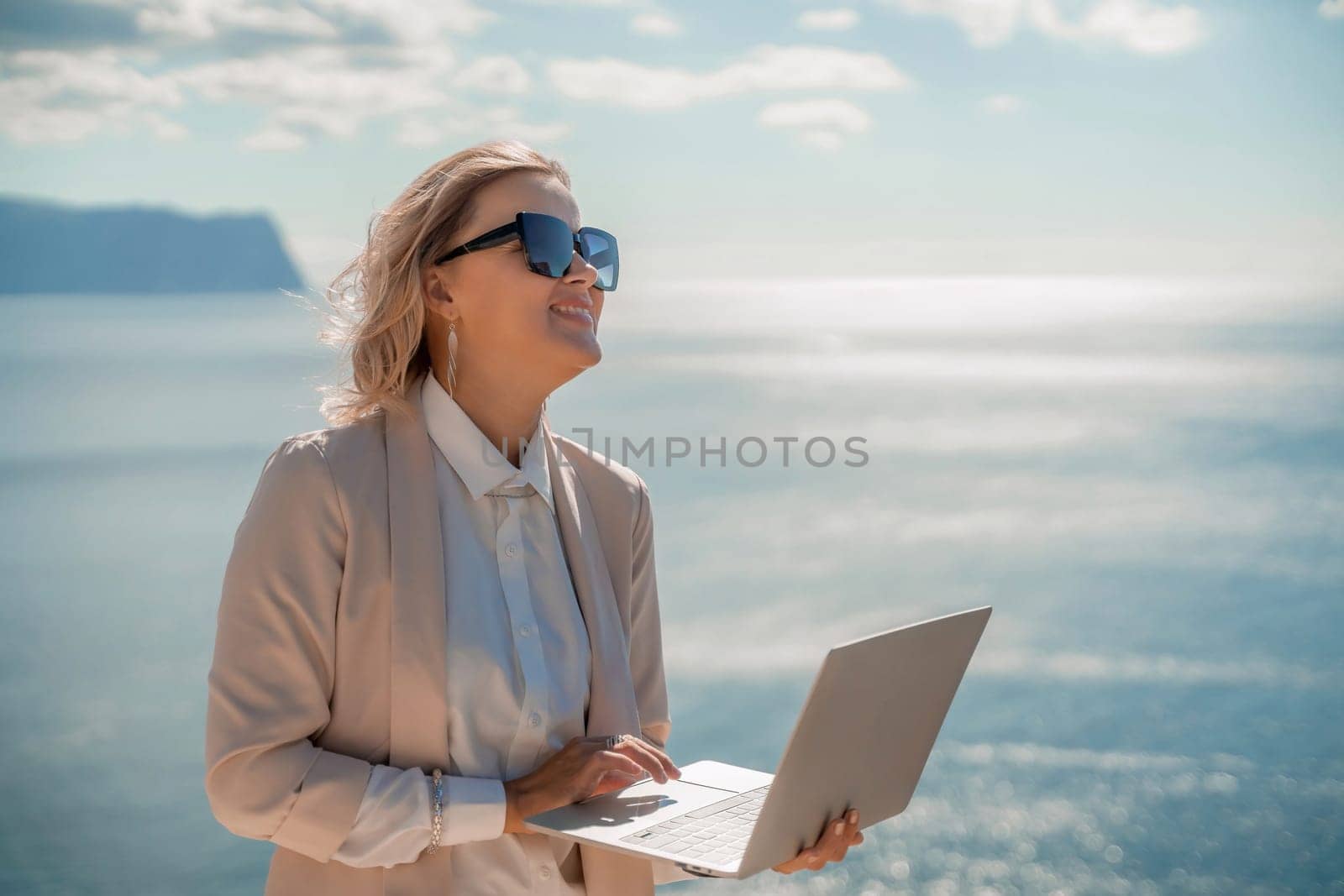Freelance women sea. She is working on the computer. Good looking middle aged woman typing on a laptop keyboard outdoors with a beautiful sea view. The concept of remote work
