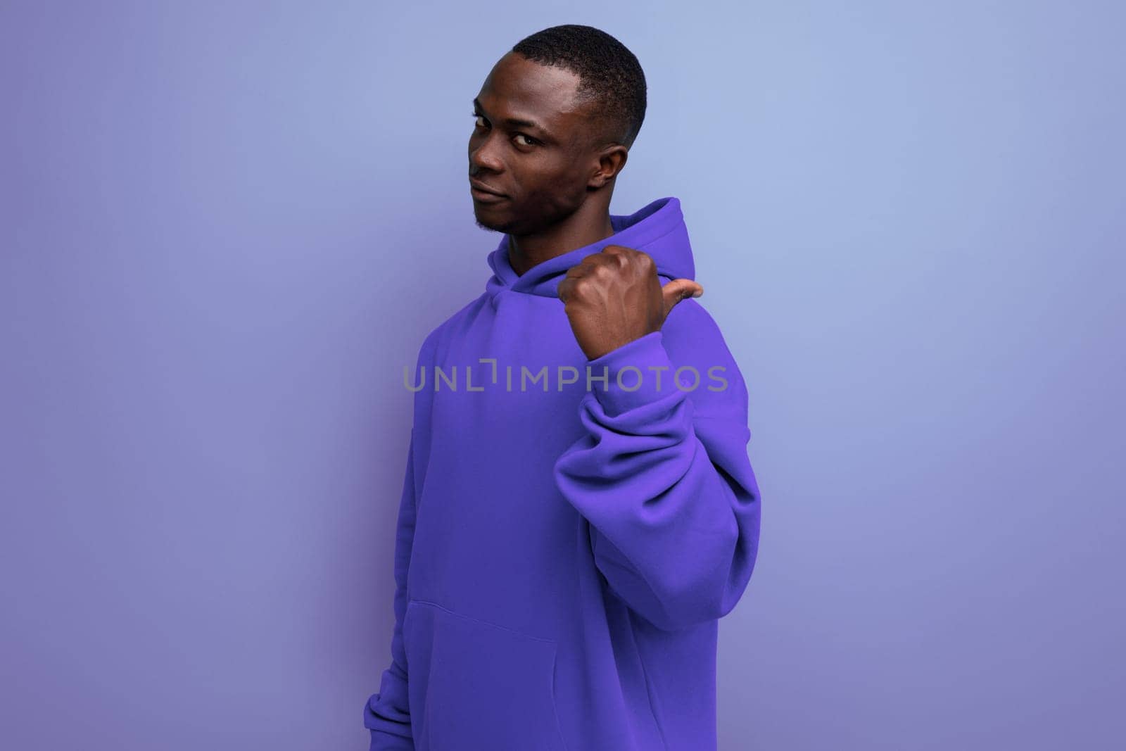 cheerful cute ethnic 25 year old african man in a stylish hoodie with a hood on a blue background by TRMK