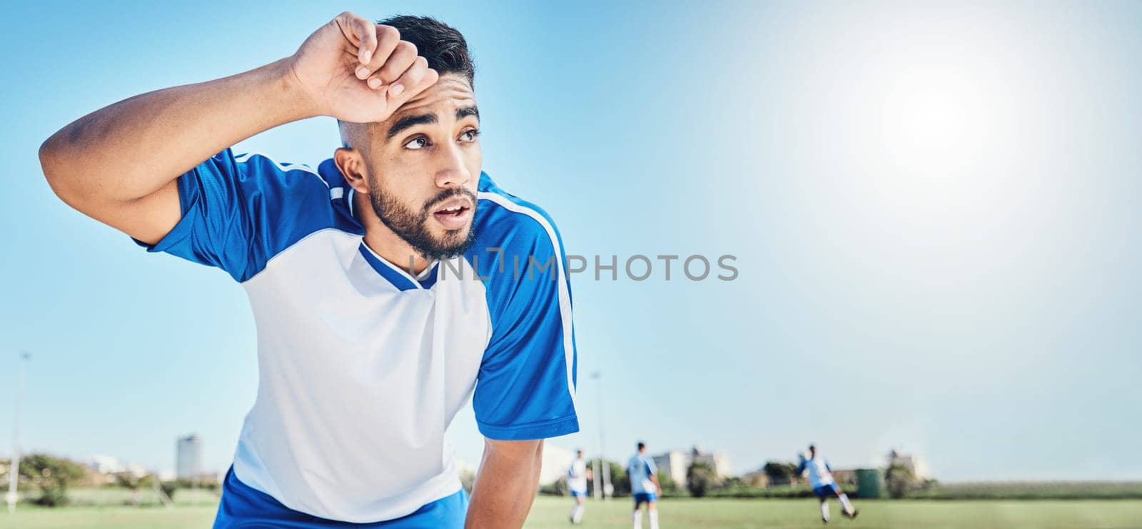 Football player, tired and man sweating outdoor on a field for sports and fitness competition. Male soccer or athlete person on a break while exhausted from training workout with mockup banner space.