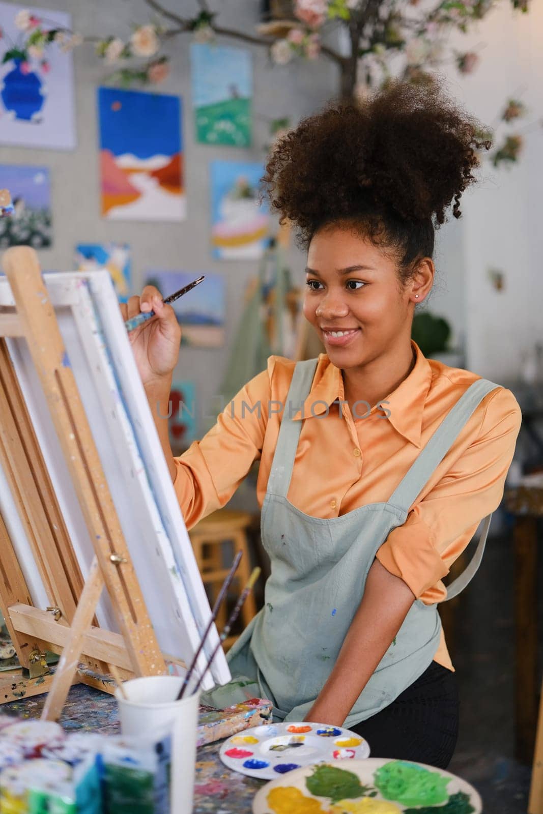 Portrait of cheerful student girl painting on canvas in art classroom. Art, creative learning and leisure activity concept.