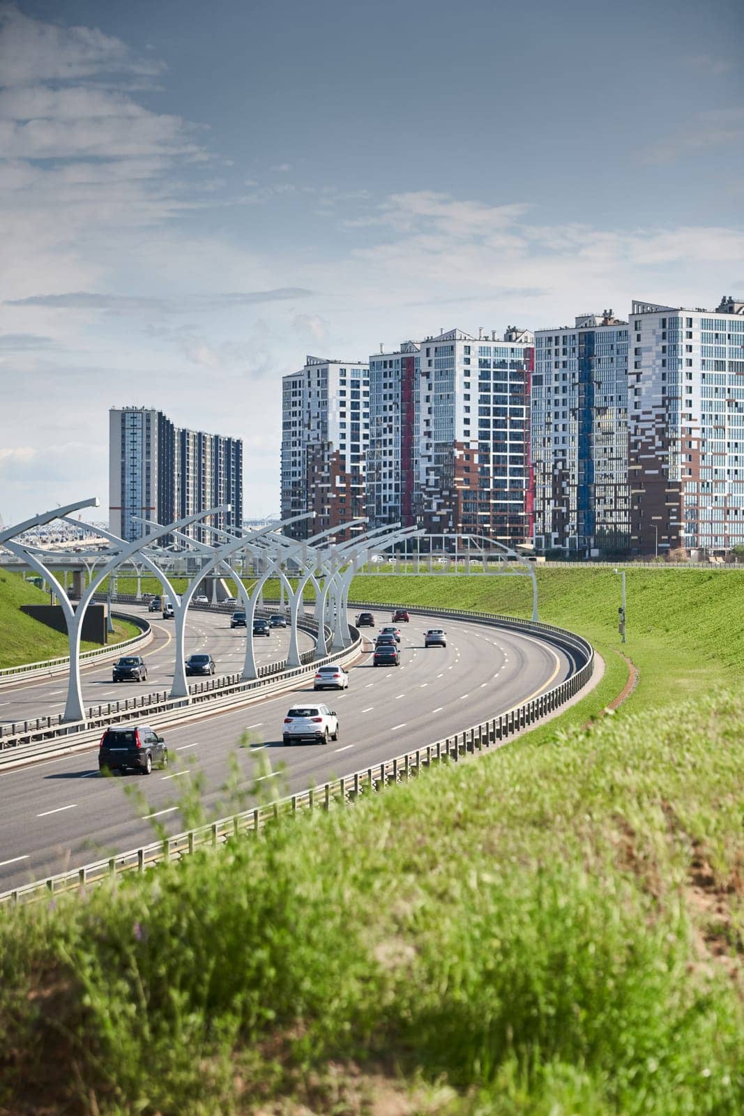 Russia, St.Petersburg, 07 July 2023: Expressway of the western high-speed diameter in clear sunny weather, green lawns along the road, new colourful residential buildings stand on a hillock, lamppost. High quality photo