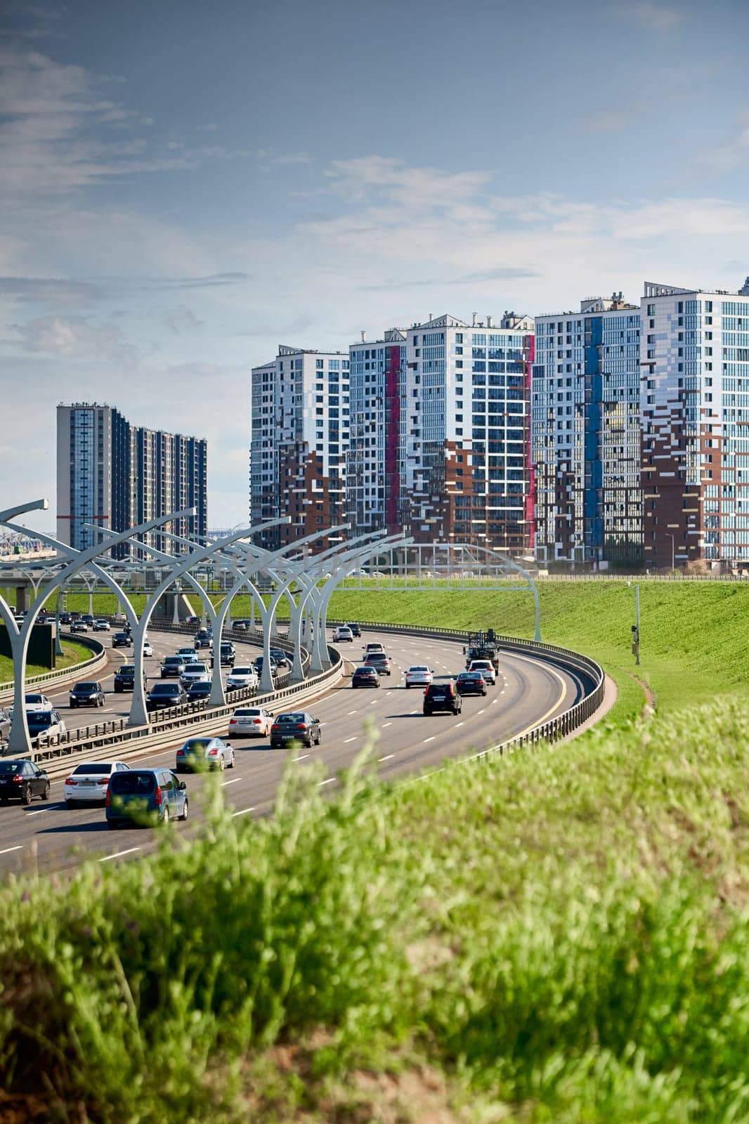 Russia, St.Petersburg, 07 July 2023: Expressway of the western high-speed diameter in clear sunny weather, green lawns along the road, new colourful residential buildings stand on a hillock, lamppost. High quality photo