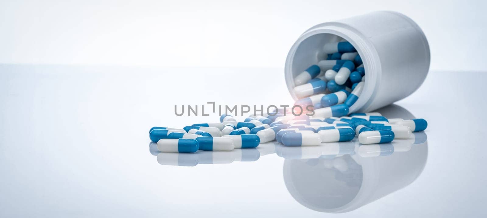 Blue-white antibiotic capsule pills spread out of plastic drug bottles. Antibiotic drug resistance. Prescription drugs. Healthcare and medicine. Pharmaceutical industry. Pharmacy product. Medication. by Fahroni