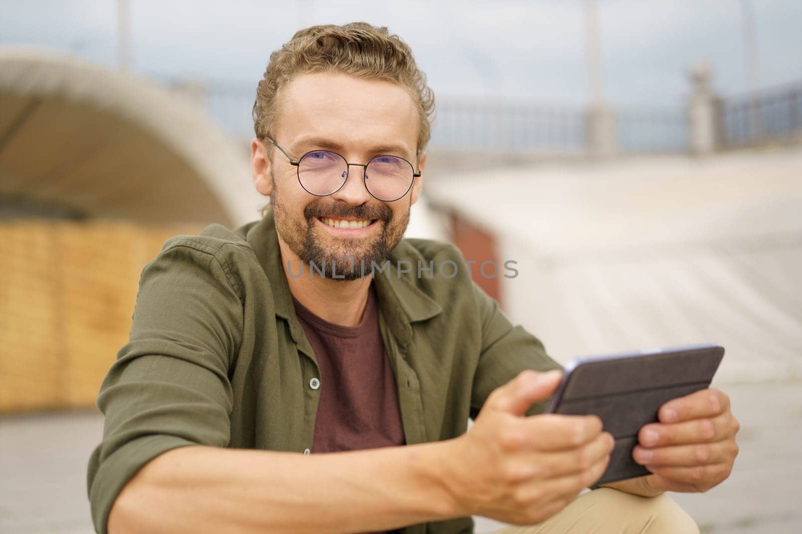 Man sitting on stairs outdoors, wearing charming smile as reads good news. With expression of pure joy and contentment, radiates positivity and happiness. . High quality photo