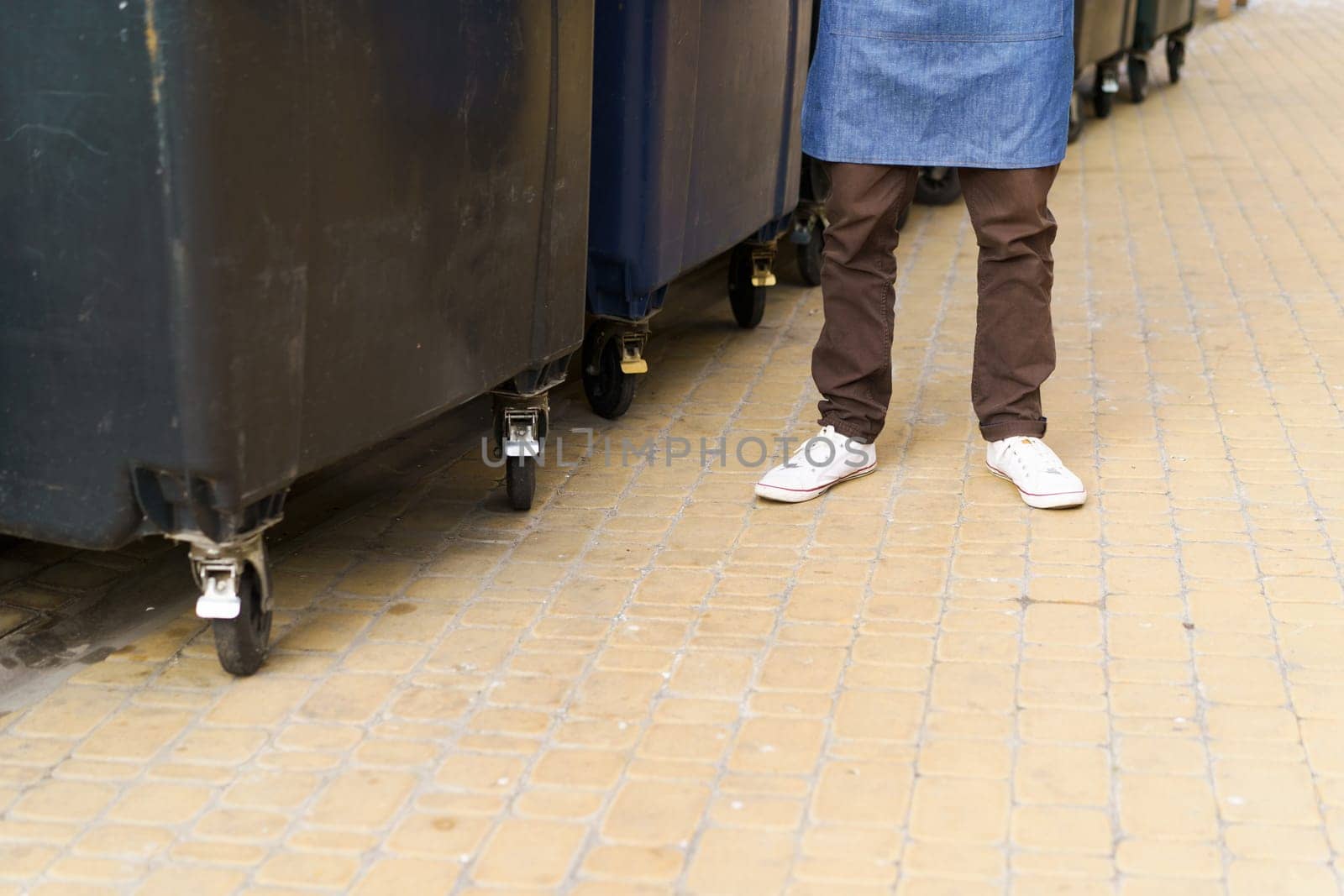 Garbage city trash cans, featuring view of trash cans in back yard and feet of kitchen worker. Presence of trash cans highlights importance of proper waste management and recycling in urban areas. by LipikStockMedia
