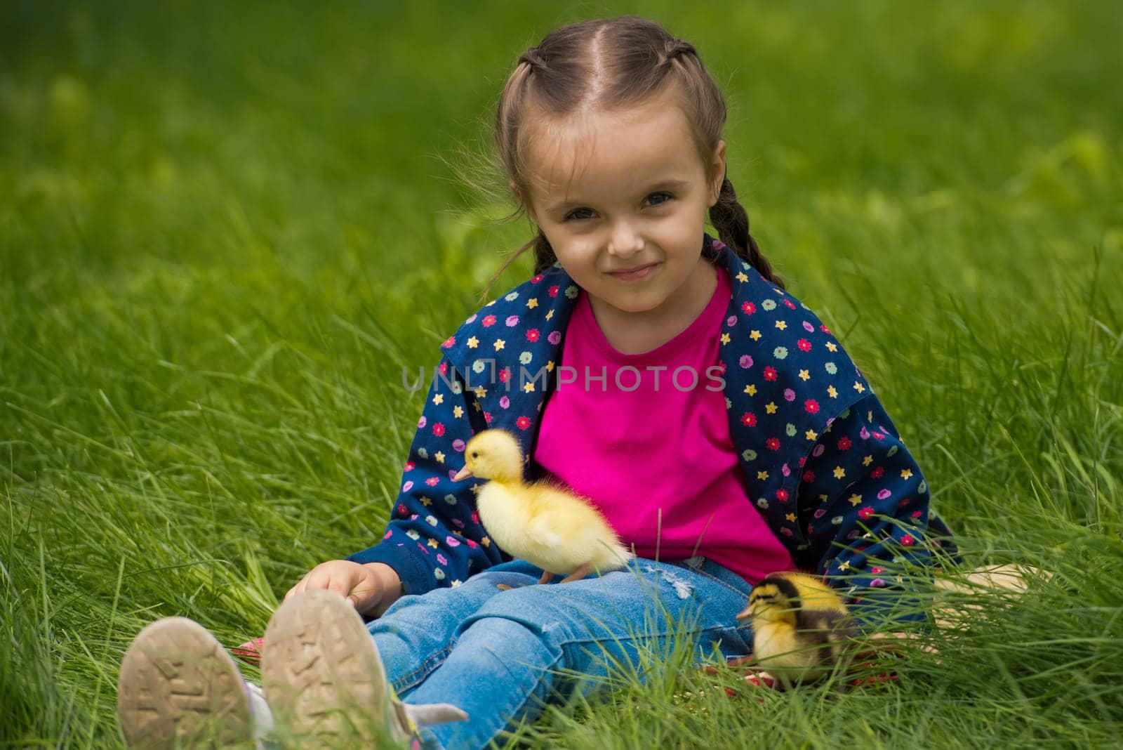 Cute happy little girl with of small ducklings in the garden. Nature background.