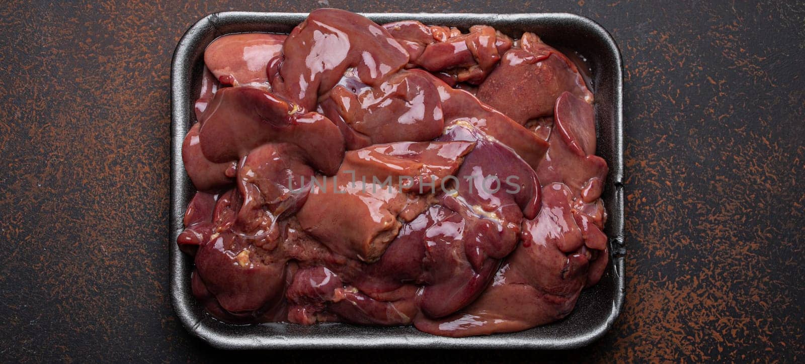 Raw chicken liver in black supermarket tray top view on dark rustic concrete background kitchen table. Healthy food ingredient, source of iron, folate and variety of vitamins and minerals by its_al_dente
