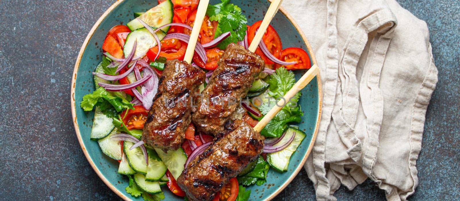 Grilled skewer meat beef kebabs on sticks served with fresh vegetables salad on plate on rustic concrete background from above. Traditional Middle Eastern, Turkish dish Kebab by its_al_dente