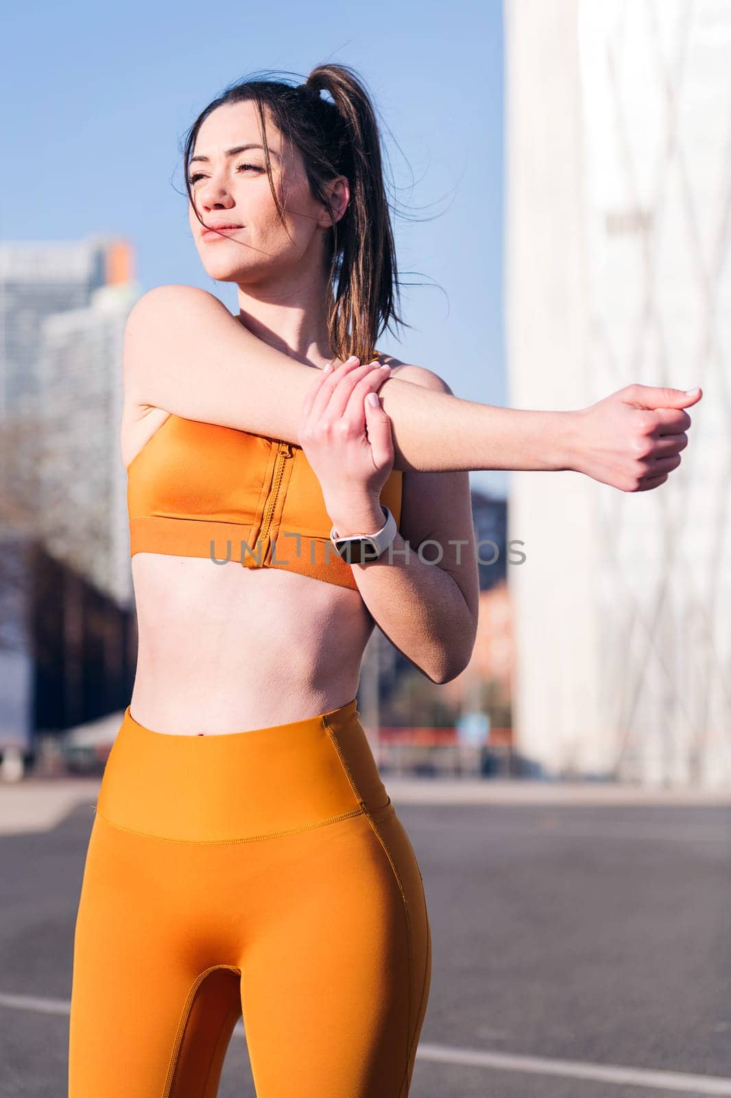 vertical photo of a caucasian fit woman stretching arms in an urban park, concept of health and sportive lifestyle
