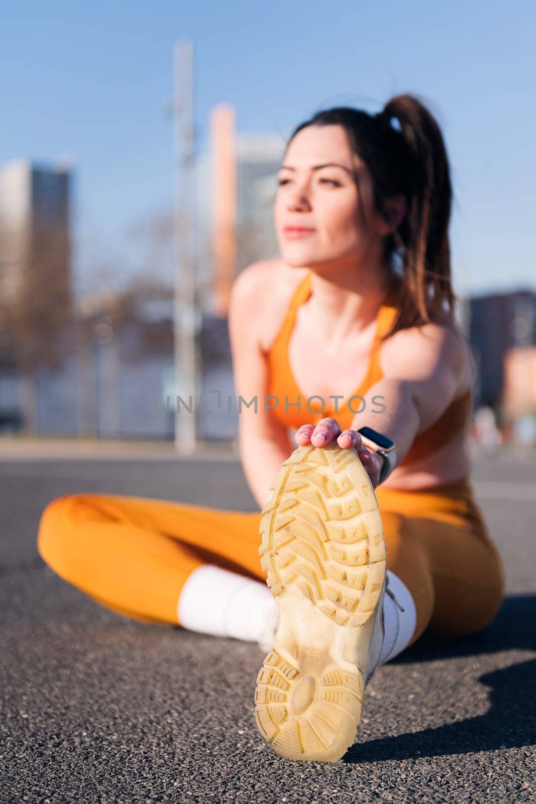 vertical photo of a caucasian woman stretching in an urban park with selective focus on the foot, concept of health and sportive lifestyle