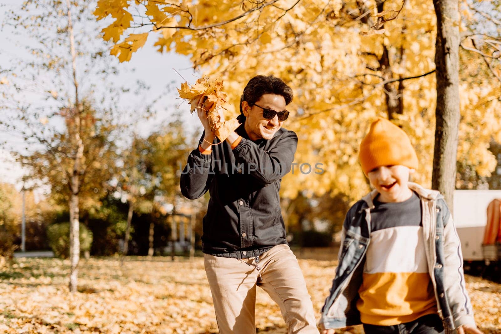 Father and son having fun in autumn park with fallen leaves, throwing up leaf. Child kid boy and his dad outdoors playing with maple leaves