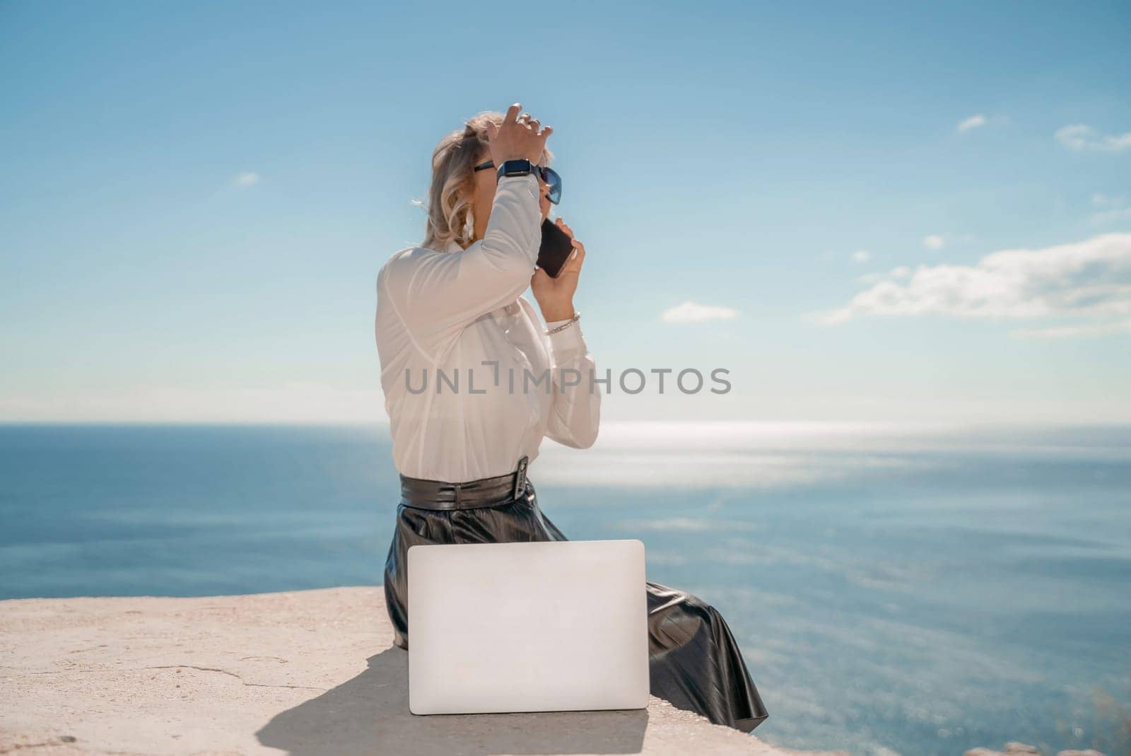 Freelance women sea working on a computer. Pretty middle aged woman with computer and phone outdoors with beautiful sea view. The concept of remote work. by Matiunina