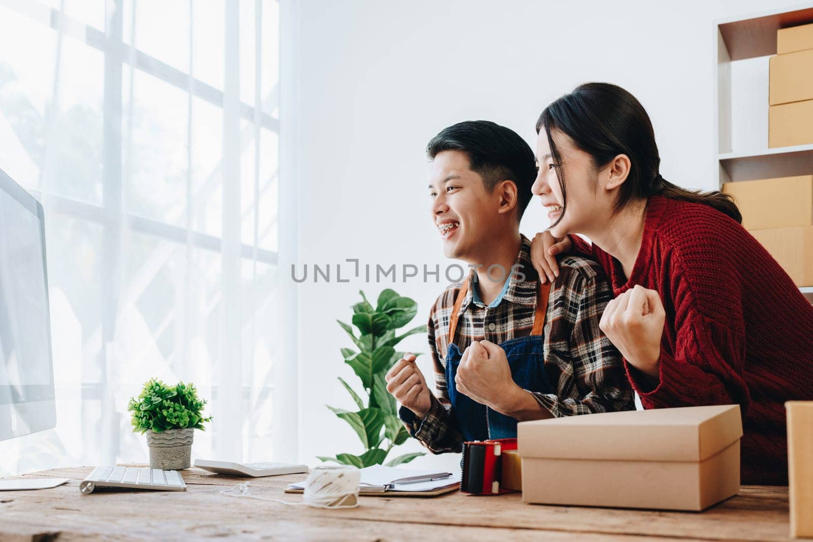 A young Asian couple shows delight and smiles on their faces when they see the sales volume and customer orders exceed expectations. sme or small business family concepts by Manastrong