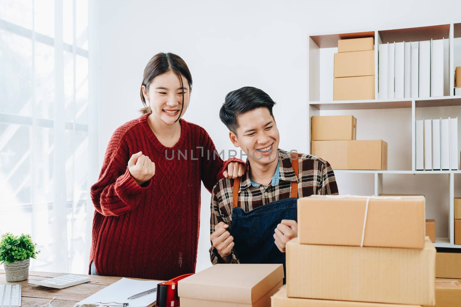 A young Asian couple shows delight and smiles on their faces when they see the sales volume and customer orders exceed expectations. sme or small business family concepts by Manastrong