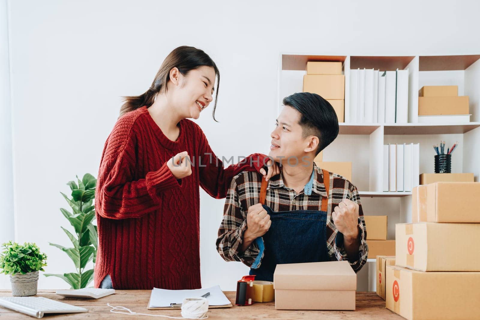 A young Asian couple shows delight and smiles on their faces when they see the sales volume and customer orders exceed expectations. sme or small business family concepts by Manastrong