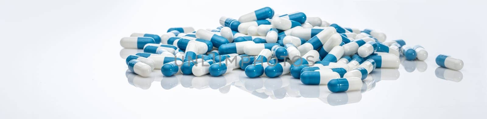 Blue-white antibiotic capsule pills on white background. Pile of antibiotic drug. Antibiotic drug resistance. Prescription drugs. Healthcare and medicine. Pharmaceutical industry. Pharmacy product.