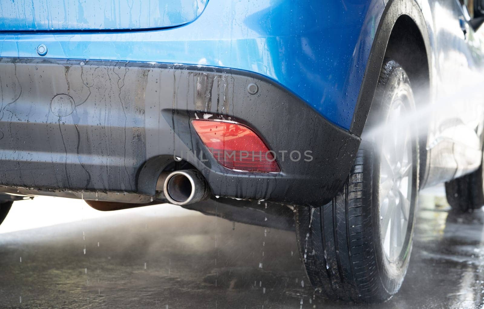 Car washing with high pressure water spray. Car cleaning. Auto care service concept. Vehicle cleaning. High pressure water spraying on car wheel and tyre. Manual car wash with high pressure water.