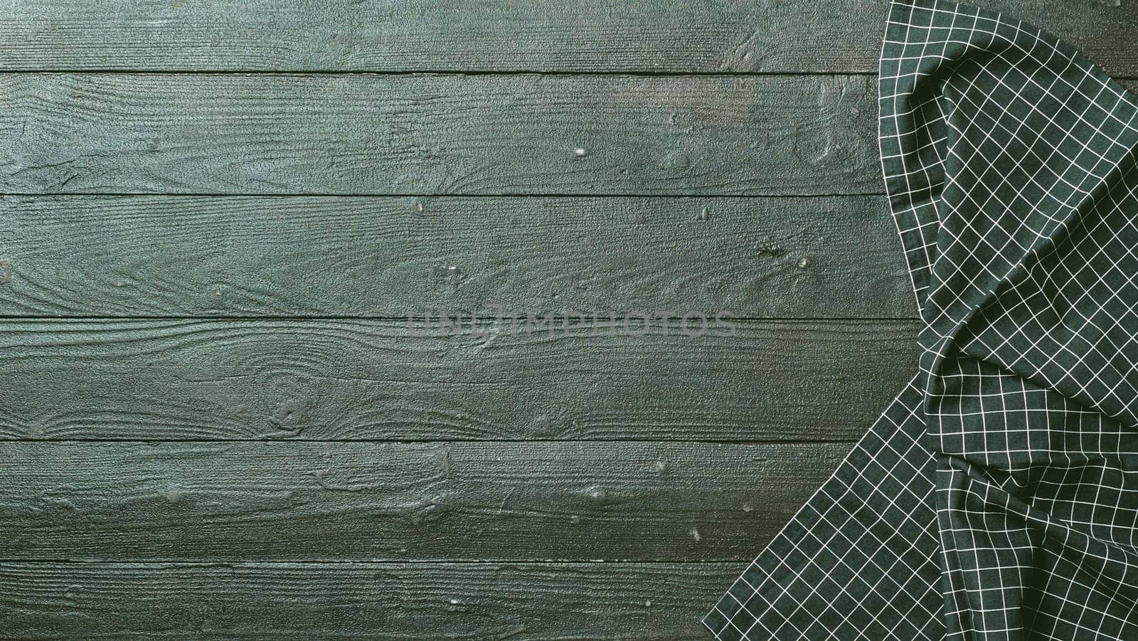 Dark wooden table with balck and white dark linen kitchen towel or textile napkin flat lay. Dark tablecloth on brown gray wood tabletop. Copy space for text. Can use as mock up for design.