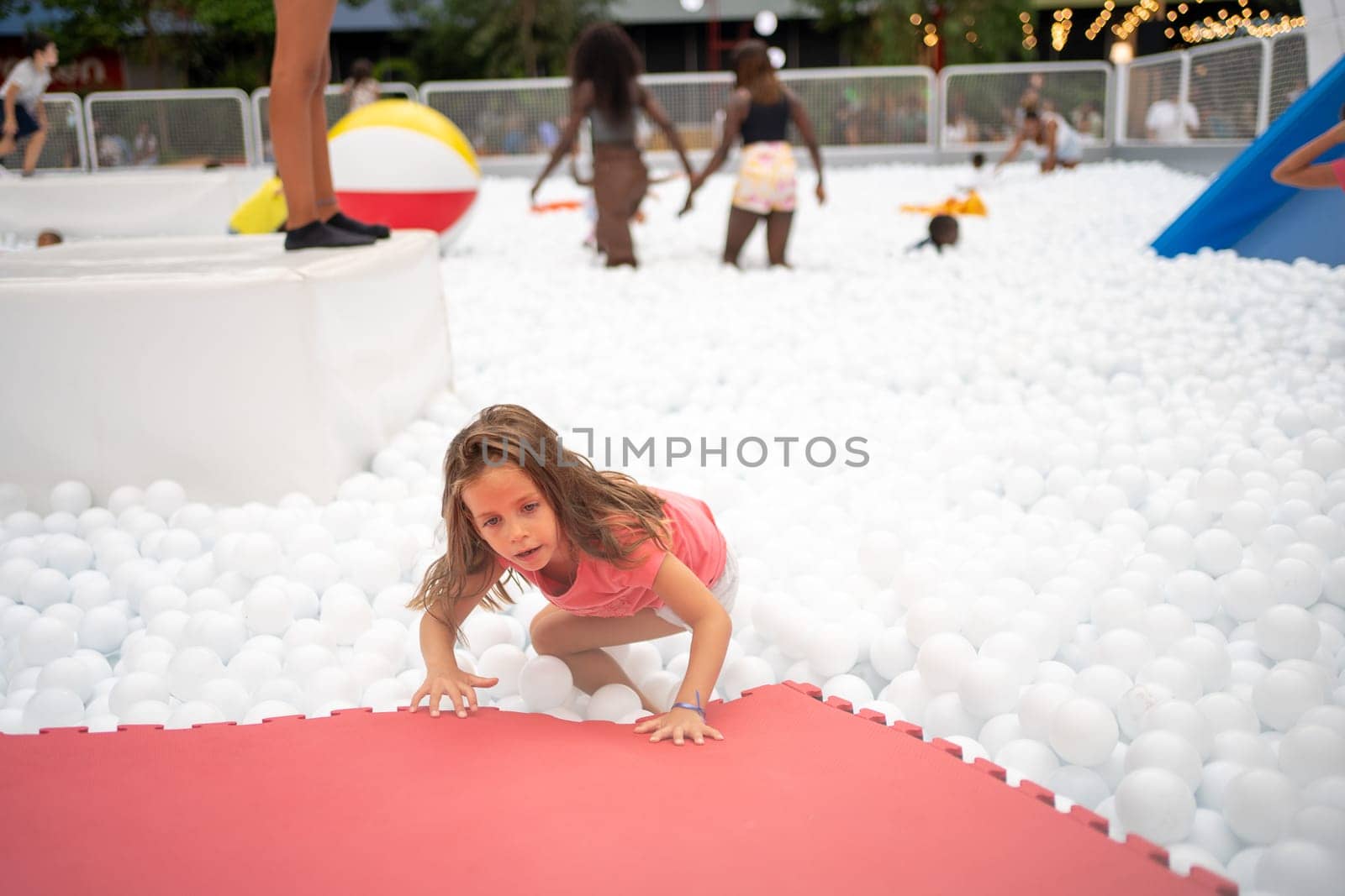 Happy little girl playing white plastic balls pool in amusement park. playground for kids. Active leisure for children.