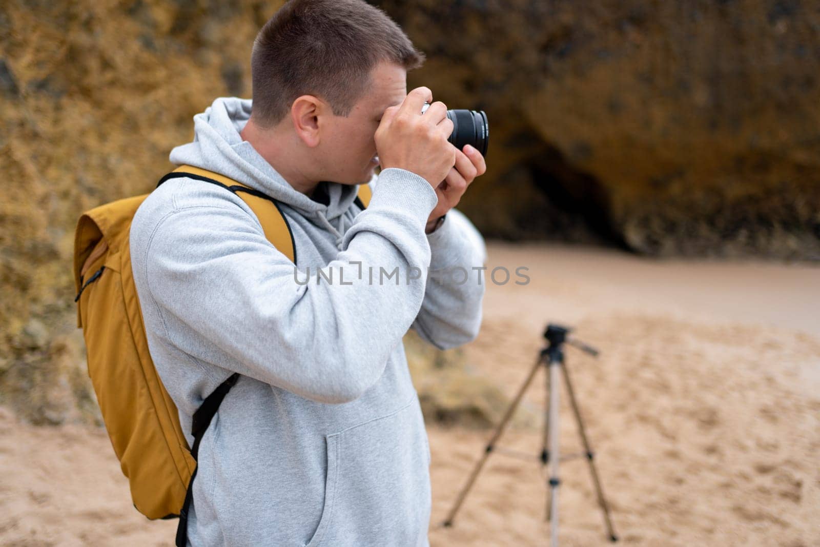 Traveler photographer takes photo beautiful seascape landscape on professional camera. Man tourist with backpack shoots a photo on beach. Side view middle shoot.