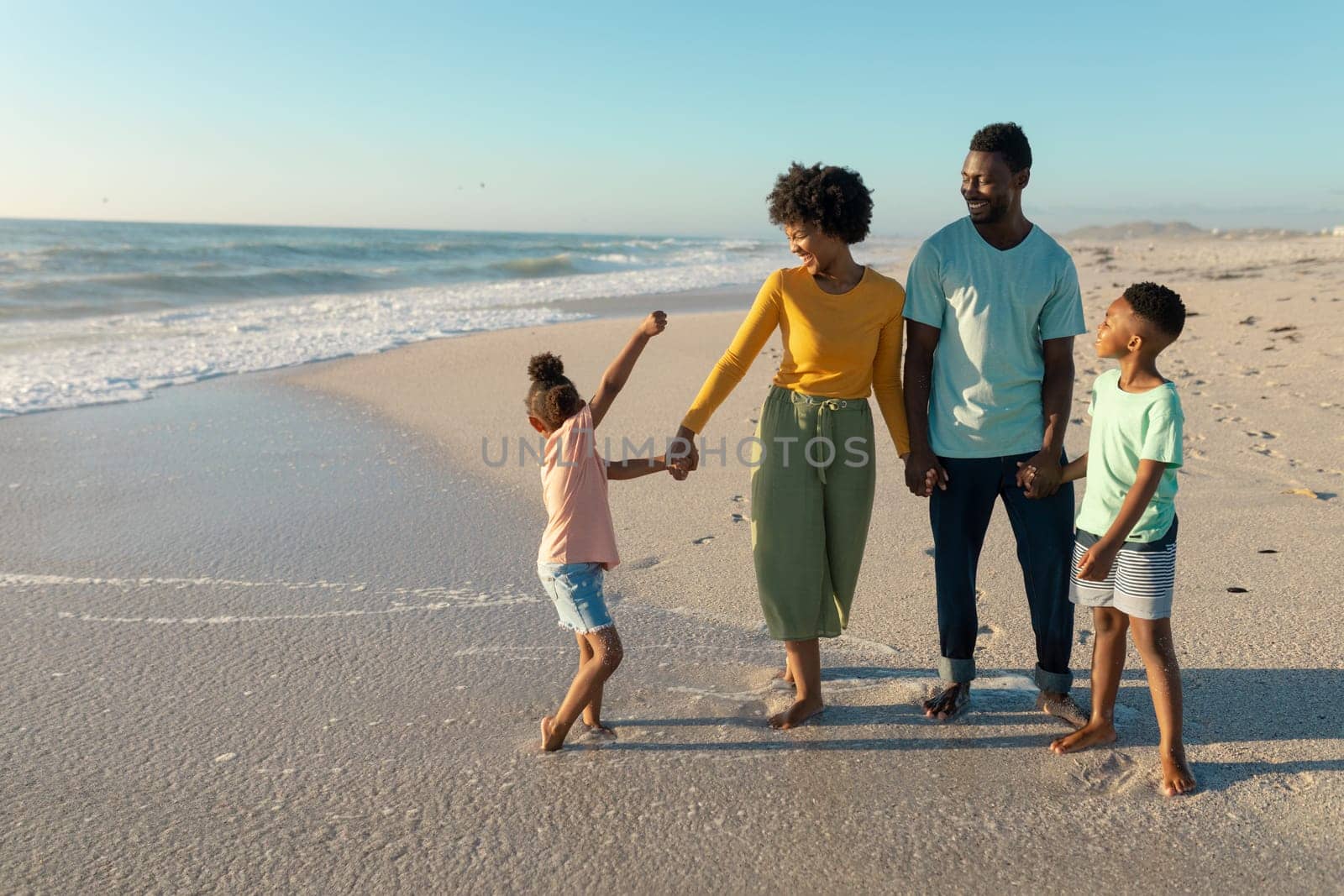 Happy african american family enjoying sunny day at beach against blue sky. unaltered, family, lifestyle, togetherness, enjoyment and holiday concept.