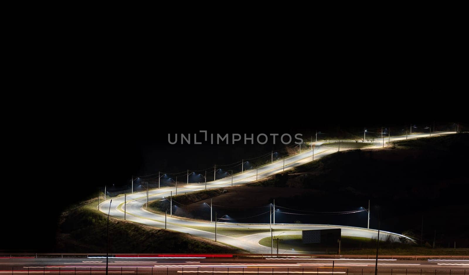 A stunning night view of a highway with long exposure light trails from passing cars. The road diversion is brightly illuminated, creating a captivating scene. The surrounding areas are dark, providing ample space for text or graphics. .