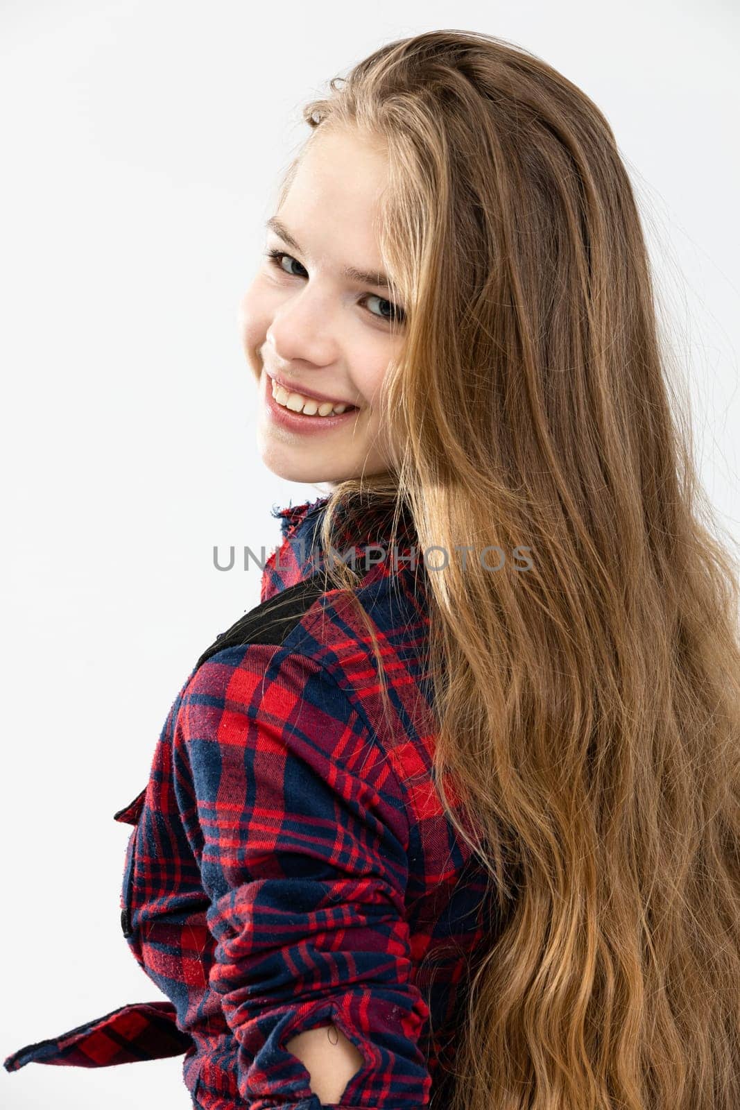 The girl turns her head back and smiles. She has long brown hair and a nice smile. She is wearing a checked shirt and her very long hair is in disarray.
