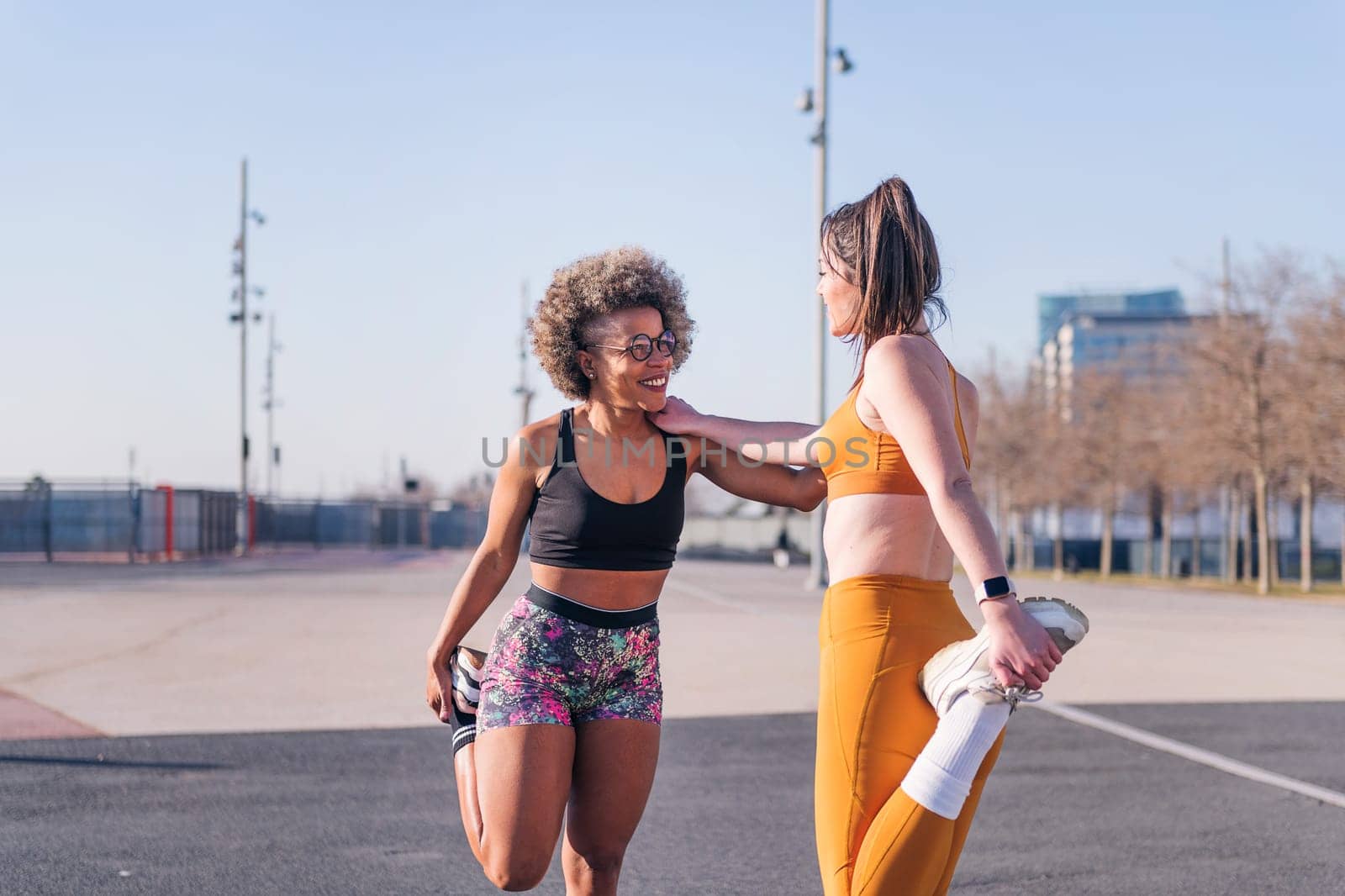 two female multiracial friends stretching together in an urban park, concept of friendship and sportive lifestyle, copy space for text