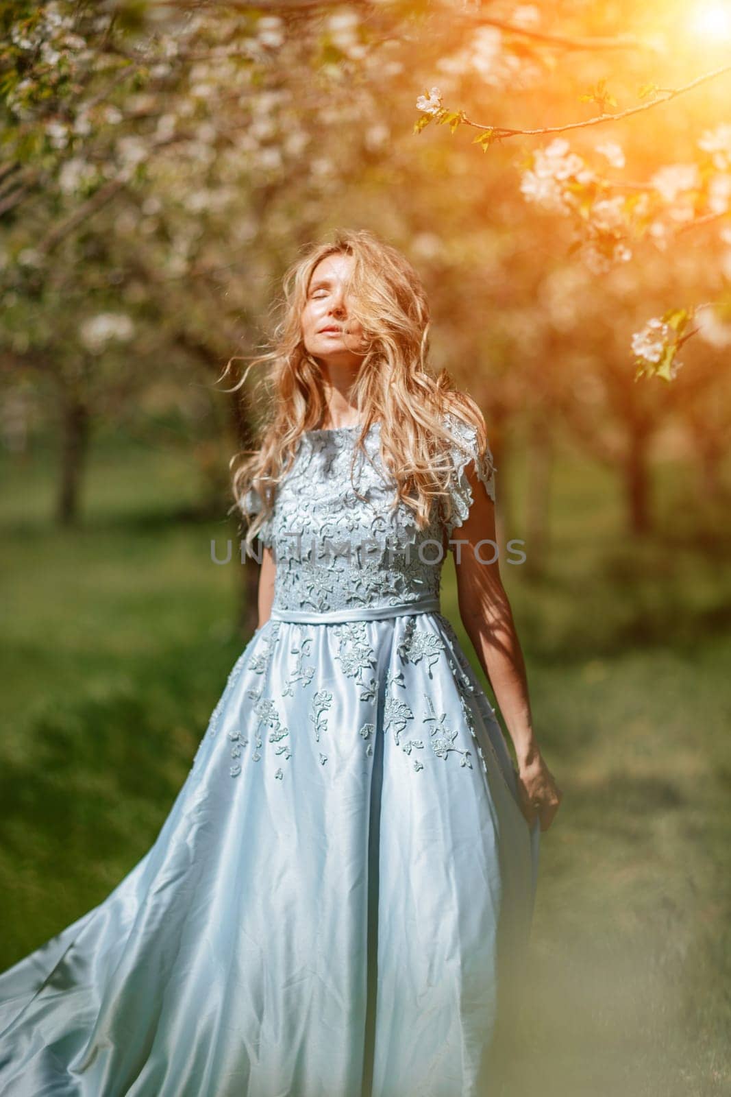 Blond blooming garden. Portrait of a blonde in the park. Happy woman with long blond hair in a blue dress. by Matiunina