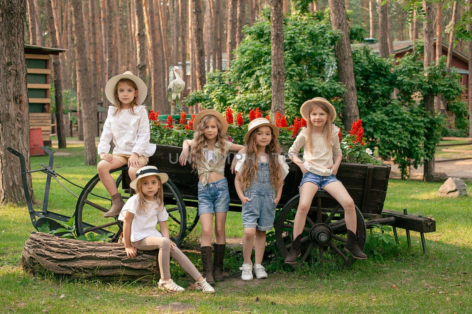 Group of friendly preteen girls posing next to vintage wooden cart designed as flower bed outdoors by nazarovsergey