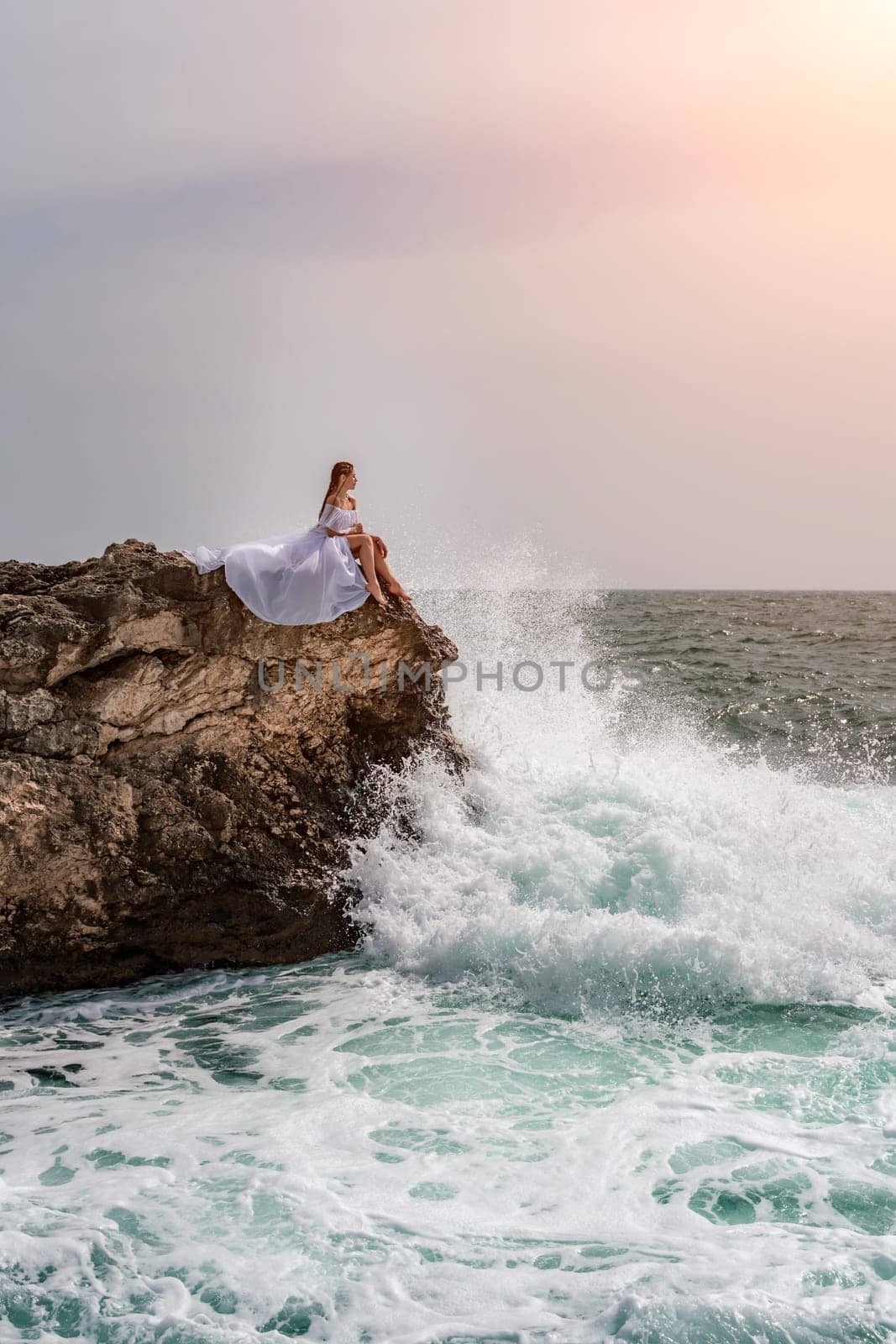 Woman sea white dress. A woman in a storm sits on a stone in the sea. Dressed in a white long dress, waves crash against the rocks and white spray rises. by Matiunina