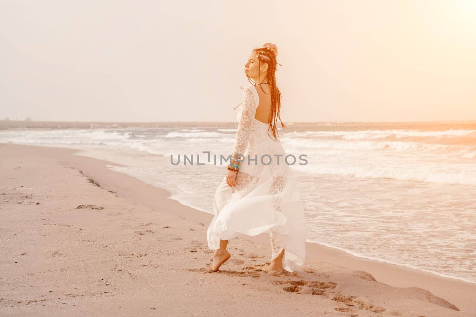 woman sea white dress. Model in boho style in a white long dress and silver jewelry on the beach. Her hair is braided, and there are many bracelets on her arms