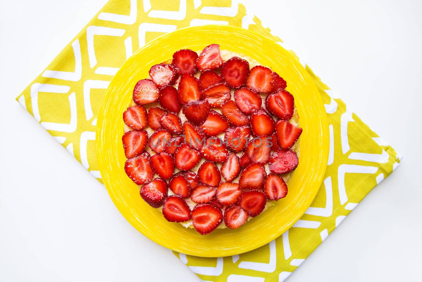 Beautiful and delicious strawberry cake stands on a yellow napkin.