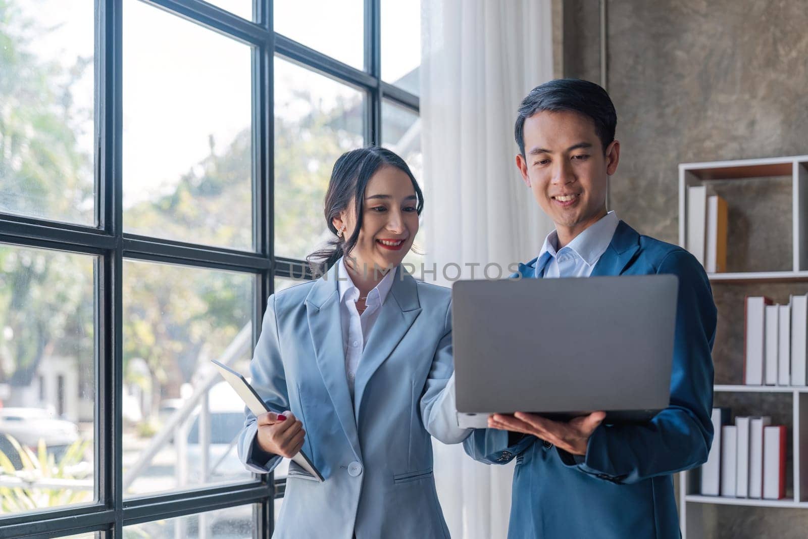 Young business man holding a laptop while discussing new project with his female collegue in office.