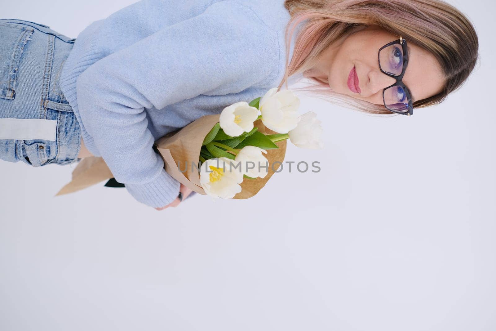Young beautiful woman holding and hugging a bouquet of white tulips. Love celebration concept. Self love concept. Woman day. Gift concept for woman celebration. Feminine. Delicate. Fragile. Copy space.