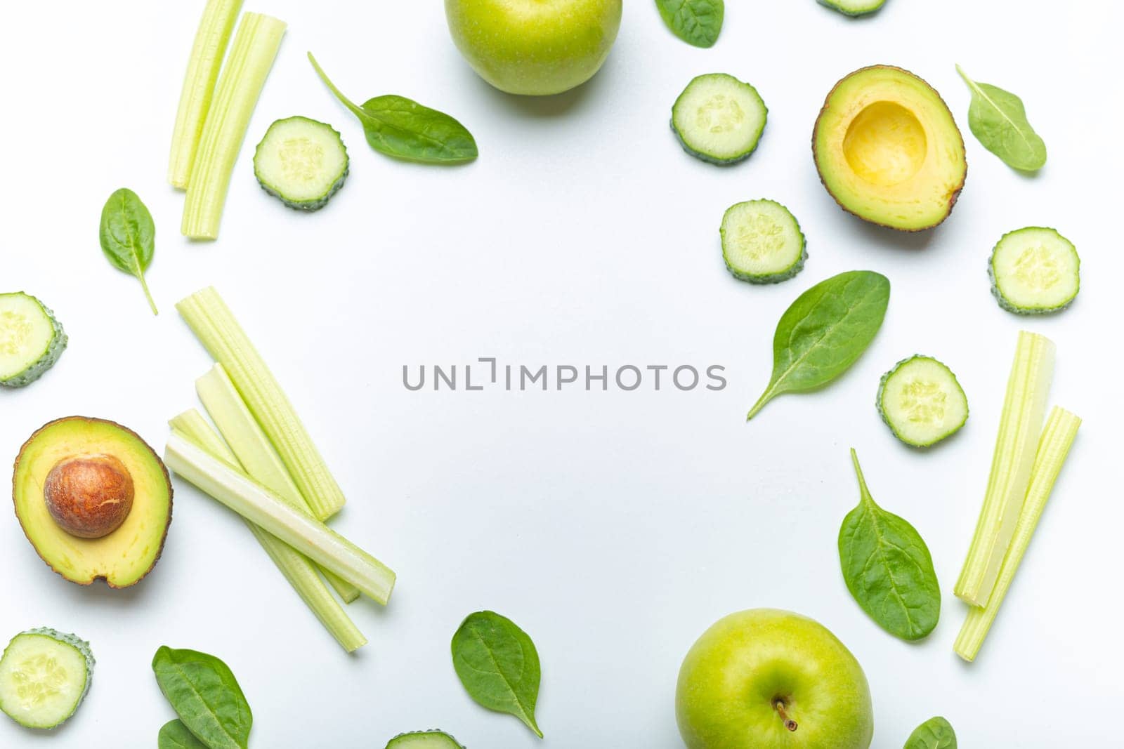 Bottle of green smoothie surrounded by green fruit and vegetables: apples, avocado, spinach, celery sticks, cucumber on white simple background top view. Diet, healthy nutrition, detox by its_al_dente