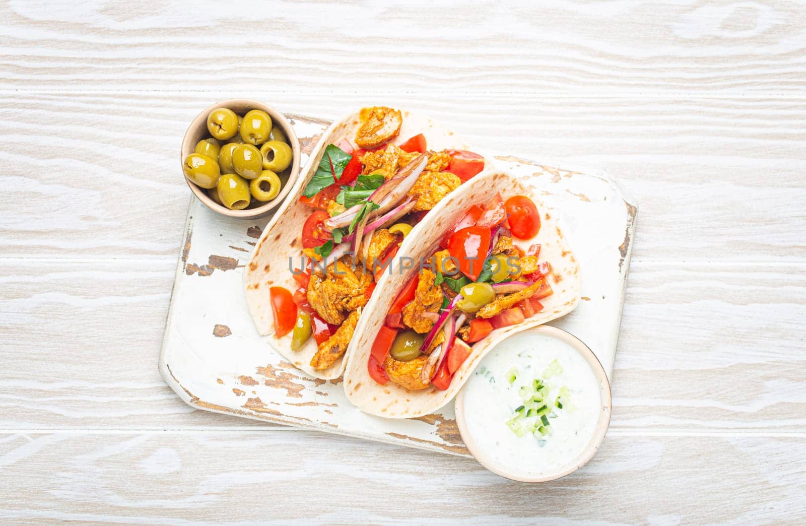 Traditional Greek Dish Gyros: Pita bread Wraps with vegetables, meat, herbs, olives on rustic wooden cutting board with Tzatziki sauce, olive oil top view on white wooden summer background. by its_al_dente