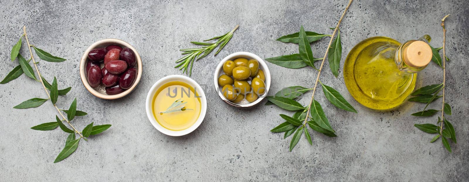 Composition with green and brown olives, extra virgin olive oil in glass bottle, olive tree branches on gray concrete stone rustic background top view by its_al_dente