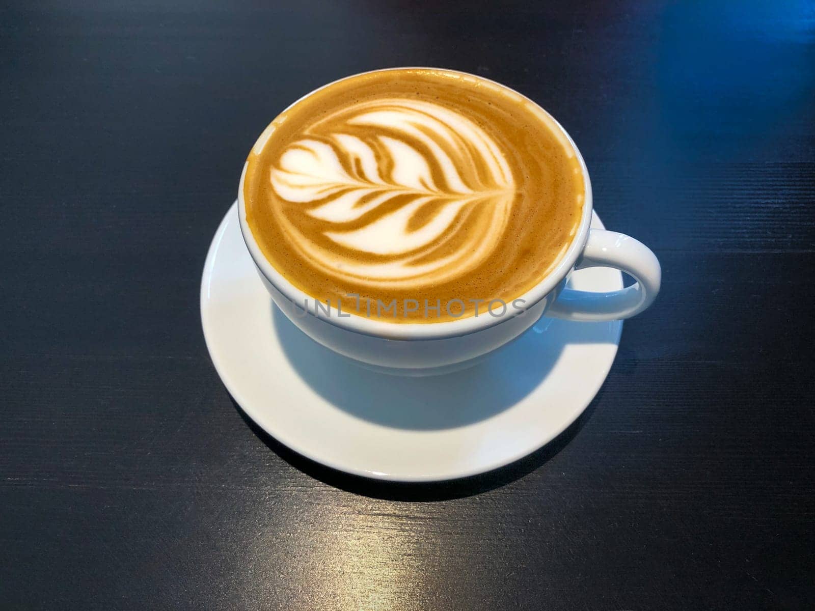 White cap of coffee latte on a black desk surface.