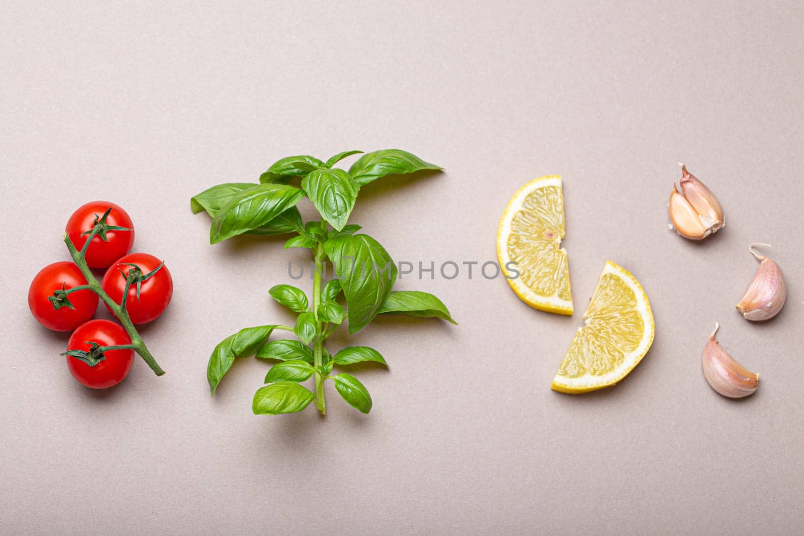 Composition with healthy food ingredients: branch of fresh cherry tomatoes, basil branch, garlic cloves, lemon wedges on minimalistic grey clean background, overhead shot by its_al_dente