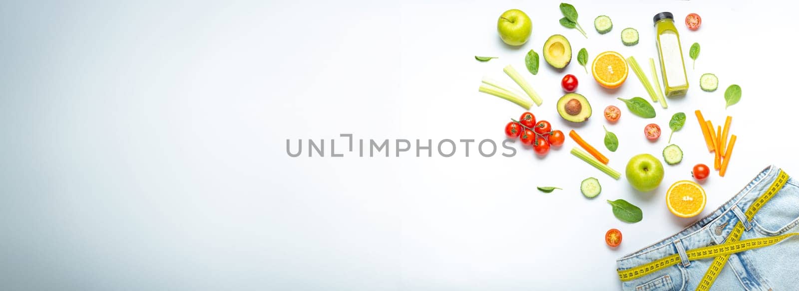 Fresh fruit, vegetables, smoothie falling into jeans and yellow measuring tape instead of belt on white background. Concept of weight loss, detox, diet, healthy clean nutrition, space for text by its_al_dente